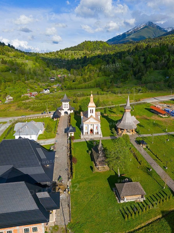 Aerial view of a church complex in a green landscape with mountain backdrop under blue sky, aerial view, Manastirea Adormirea Maicii Domnului, Izvorul Negru, Moisei monastery, Maramure?, Maramures, Maramures region, Romania