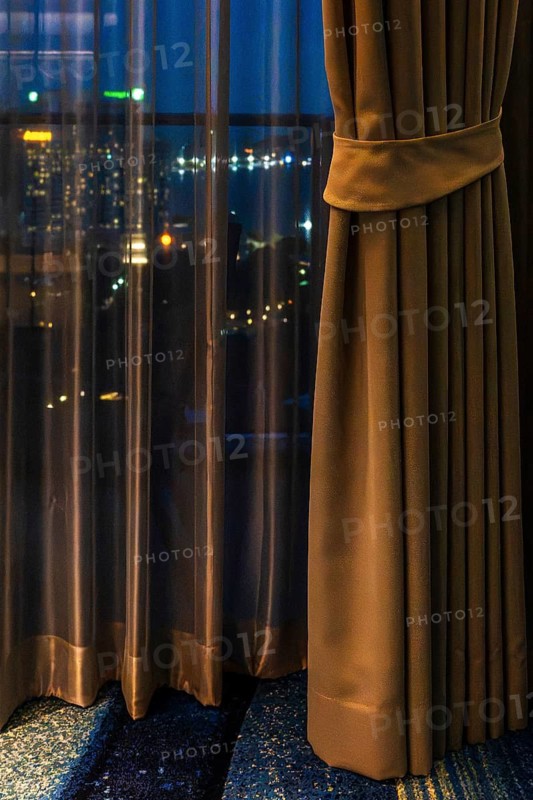Hotel room view through curtain illuminated city scenery, Pattaya, Thailand