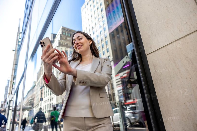 Young businesswoman smiling while interacting with her mobile phone on a vibrant manhattan city street, reflecting urban life and modern communication in an outdoor setting
