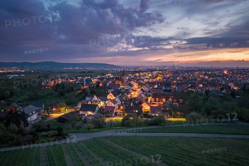 City skyline at night illuminated under a dramatic sky with a view of surrounding vineyards, Korb im Rems Valley, Baden-Württemberg, Germany