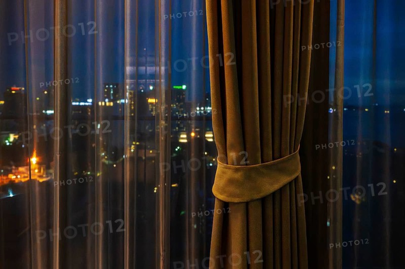 Hotel room view through curtain illuminated city scenery, Pattaya, Thailand