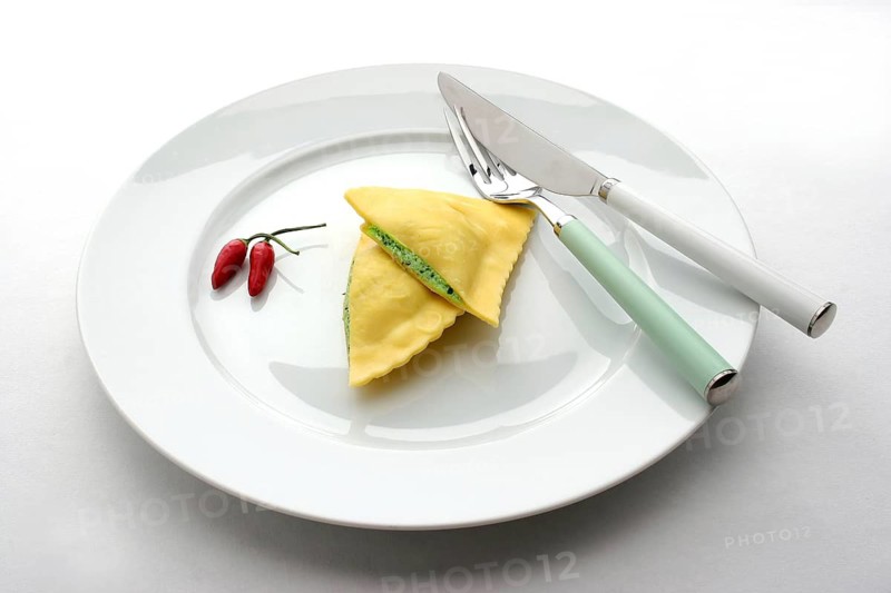 A white plate with two ravioli, dumplings, pasta, peppers, knife and fork, studio photo, Austria