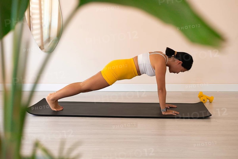 Woman in plank with plants and sunlight creating a serene workout space