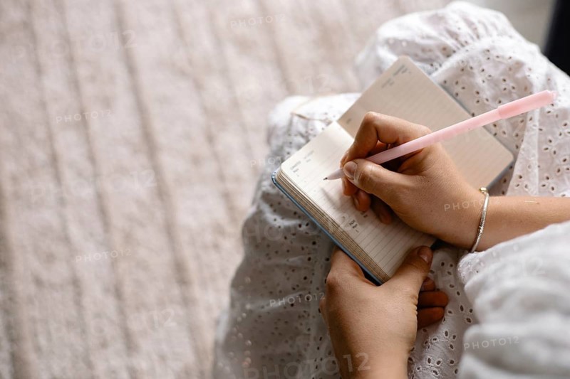 A person writes in a notebook while sitting on a carpet, conveying a relaxed atmosphere
