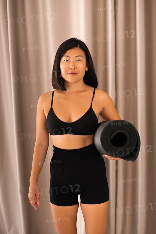 Woman standing with a yoga mat in fitness wear, exuding confidence indoors