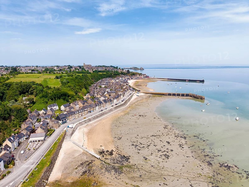 Aerial view of the picturesque fishing village of Cancale on the Emerald Coast. The picture shows the Port de la Houle harbour area at low tide with the distinctive Cale de l'Épi pier. The row of houses with numerous fish restaurants stretches along the shore. The region is world-famous for its oyster farming. In the background you can see Mont-Saint-Michel Bay, Ille-et-Vilaine department, Brittany, English Channel, France