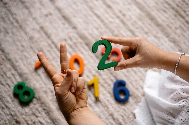 Hands displaying a peace sign and holding a green number two over a rug with numbers