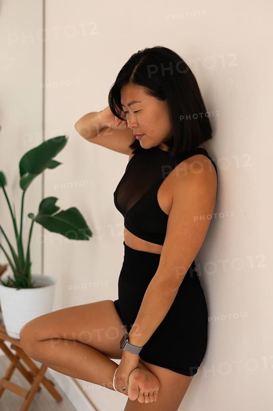 Woman in a seated yoga pose with a calm expression, leaning against a studio wall