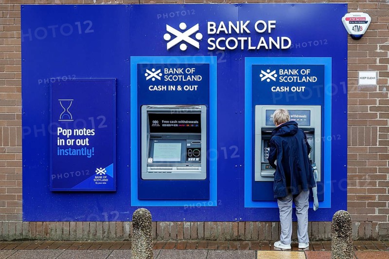 Woman using an outdoor Bank of Scotland ATM to withdraw cash on a street in Partick, Glasgow, Scotland, United Kingdom