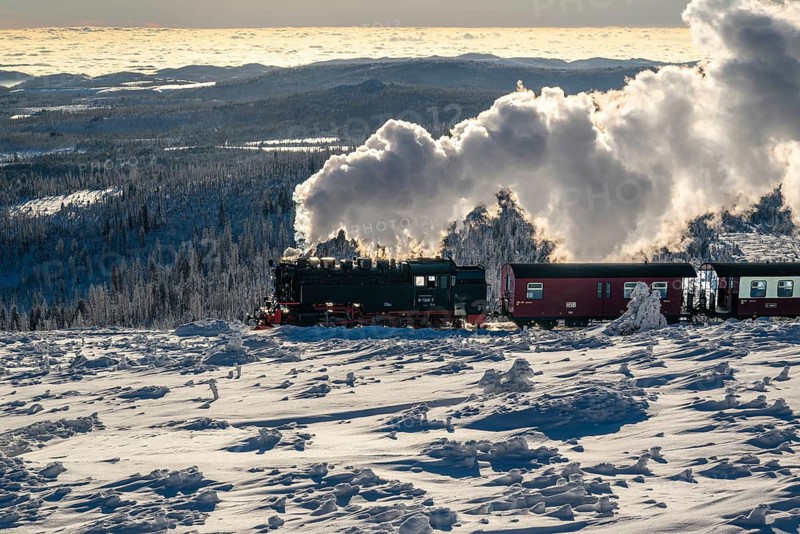 The Brocken Railway with steam locomotive in atmospheric backlight on the way to the snow-covered and ice-covered summit of the Brocken, with the vast winter landscape in the background, Harz National Park, Saxony-Anhalt, Germany