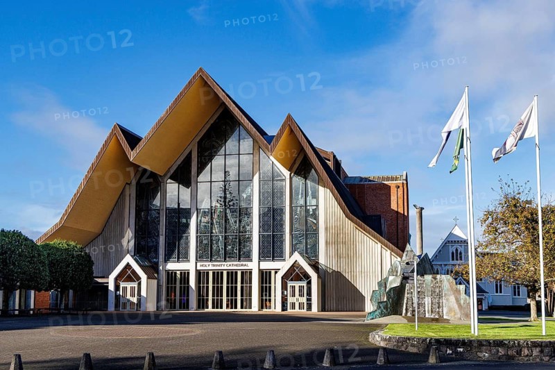 Holy Trinity Cathedral, Auckland, with dramatic angular modernist facade, large glazed gable window and flags under blue sky, Auckland, New Zealand