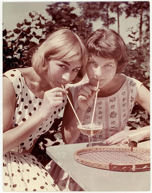 Summer, young girls drinking spritzer, out of a glass, Berliner Weisse, tennis, two woman drinking through straws from glasses outdoors, relaxed summer atmosphere. Ludwig Harren, 1960
