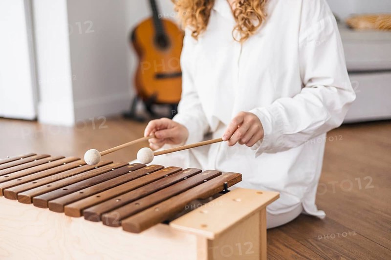 Person playing marimba on a wooden floor, focusing on the instrument