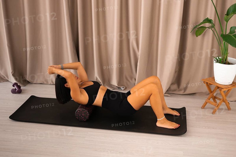 Woman lying on a foam roller with stretched arms on a yoga mat in a serene atmosphere