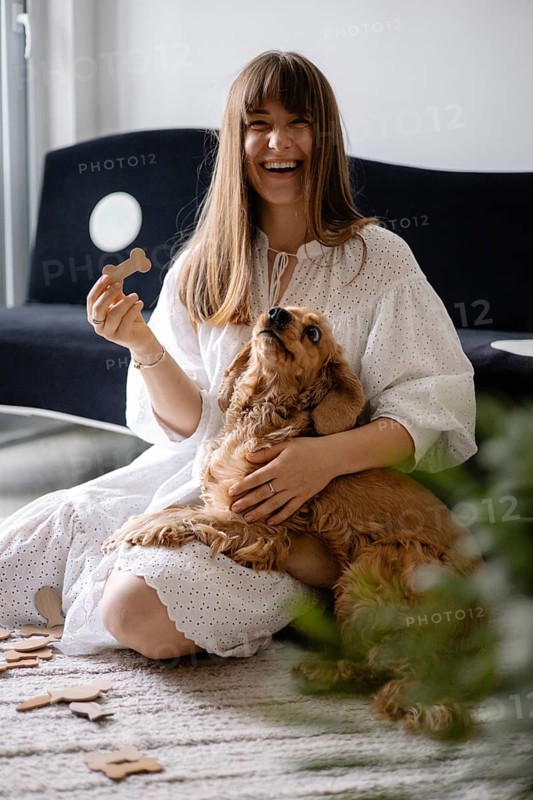 Woman in a white dress smiling with a dogcocker spaniel at her side, holding a puzzle piece