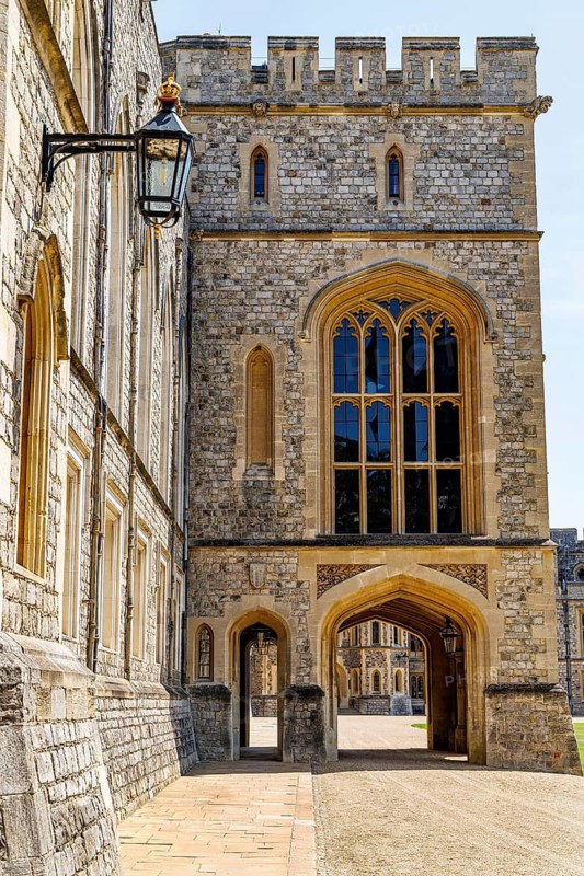 A crenellated gatehouse tower pierced by a large Gothic traceried window overlooks a smaller archway in Windsor Castle's Upper Ward, part of the ceremonial buildings enclosed by the castle's medieval defensive walls, Windsor, England, United Kingdom