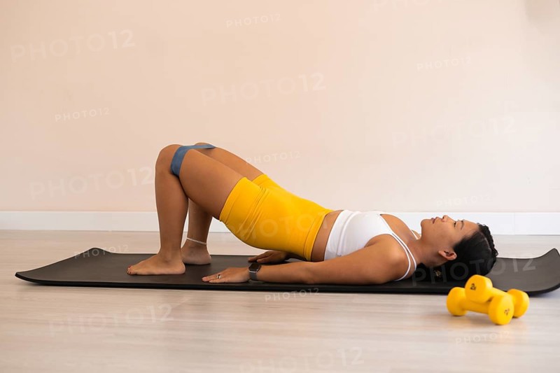 Woman performing a glute bridge with resistance band on a mat indoors