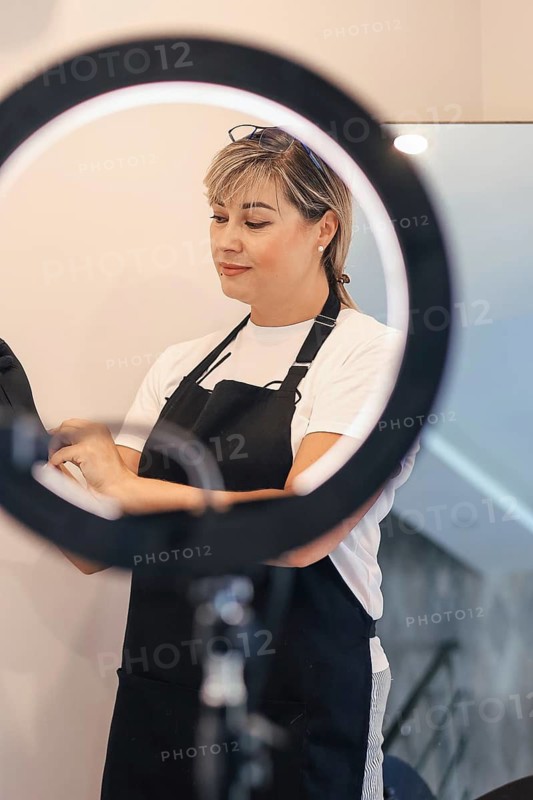 Woman adjusting gloves under a ring light, wearing an apron, appears focused, professional atmosphere