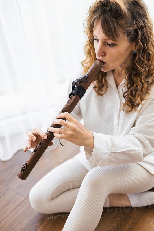 A woman with curly hair playing a flute, captured in a moment of focus