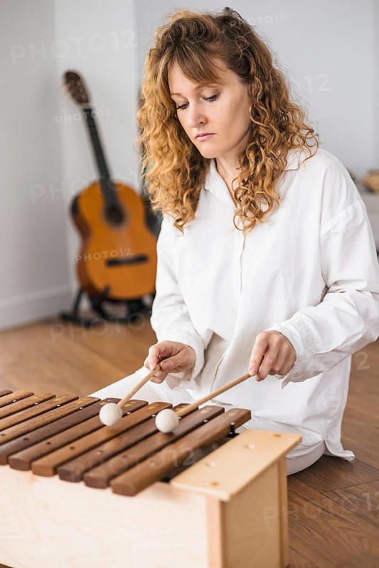 Woman playing marimba with a guitar in the background on a wooden floor