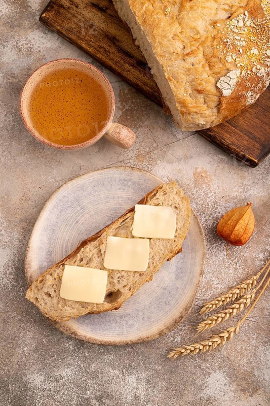 Slice of homemade bread with butter on plate on brown concrete background, cup of tea, close up, top view, flat lay