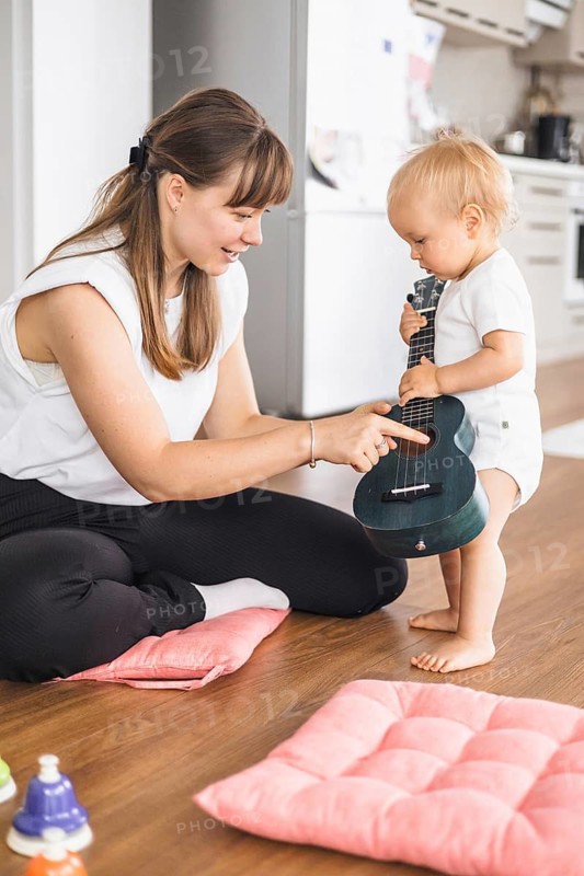 A mother guides her toddler during a playful music session with a ukulele