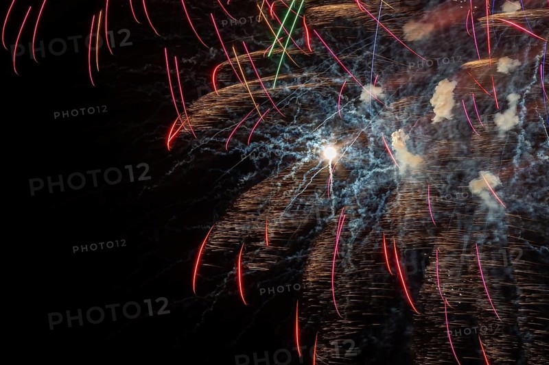 Red, orange and golden fireworks plus puffs of white smoke light up a black sky at night in summer, Quebec, Canada