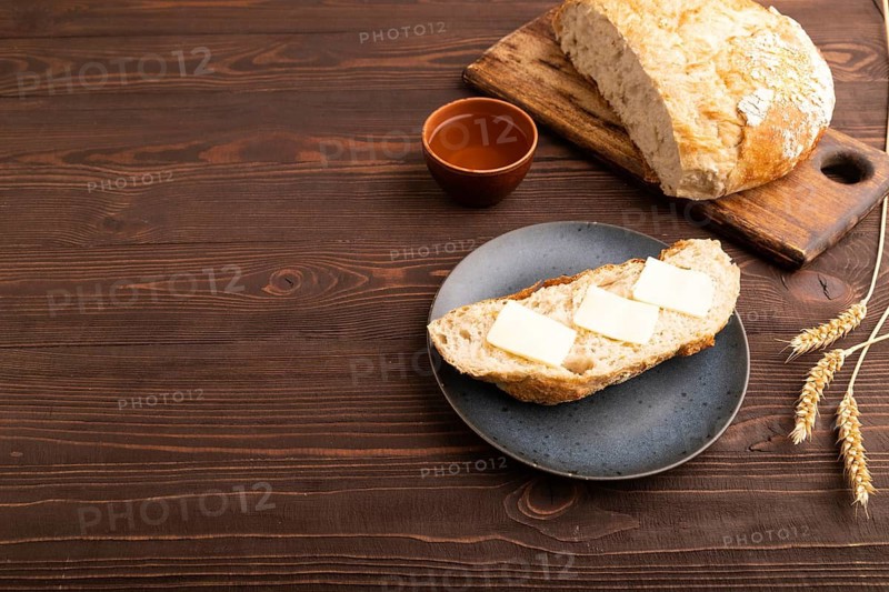 Slice of homemade bread with butter on plate on brown wooden background, cup of tea, copy space, side view