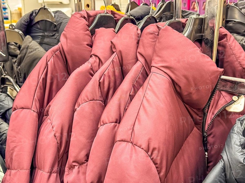 A row of puffy jackets in various colors hanging on a rack. The jackets are designed for winter wear, showcasing a cozy and warm appearance