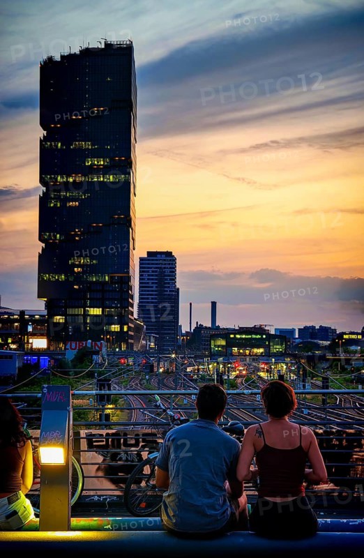Romantic scene, view from Modersohn Bridge towards EDGE East Side high-rise building, evening atmosphere with a couple on a bridge at sunset and view of the skyline, Friedrichshain, Berlin