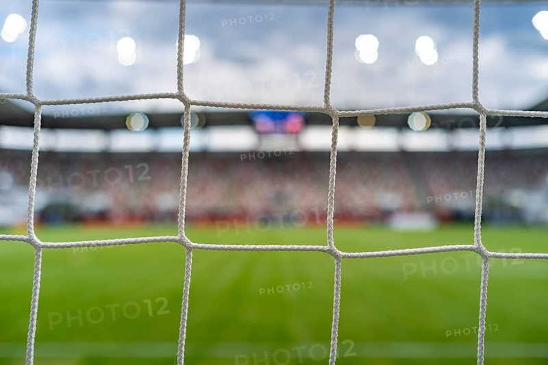 Soccer goal net in the foreground with a blurred football field, stadium and spectators in the background, representing competition, sport and victory in Lubin, Poland