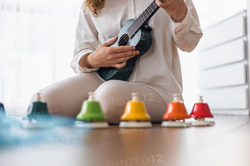 A woman in white playing a ukulele surrounded by colorful bells