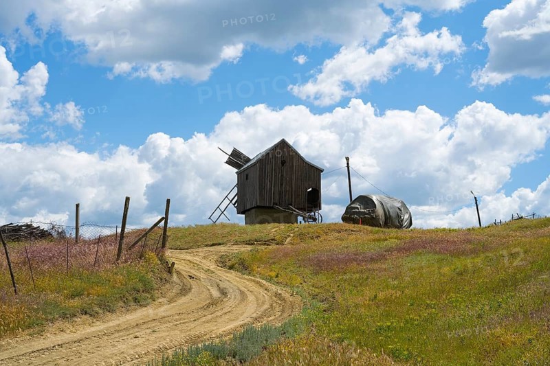 Dirt road leads to a wooden windmill on a hill under blue sky with clouds surrounded by nature, windmill, Besalma, Be?alma, Comrat district, Gagauzia autonomous region, Republic of Moldova, Moldova