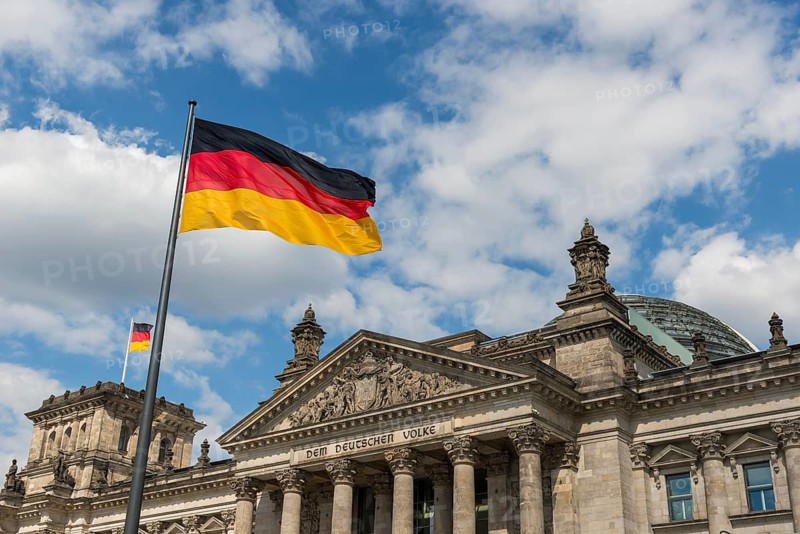 German flags are blowing in the wind in front of the German Reichstag in sunshine and blue sky, Berlin