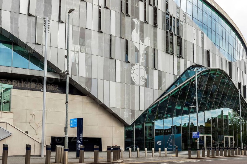 The club crest patterns the cladding above a glazed entrance canopy at Tottenham Hotspur Stadium, London, England, United Kingdom