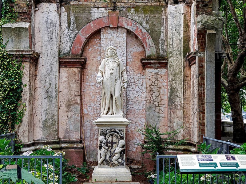 An inscribed plinth carries a marble statue of Sir Robert Clayton, benefactor and President of St Thomas Hospital, set within a weathered, cracked archway on the North Wing. Cherub carvings decorate the base of this Grade I listed monument by Grinling Gibbons, London, England, United Kingdom