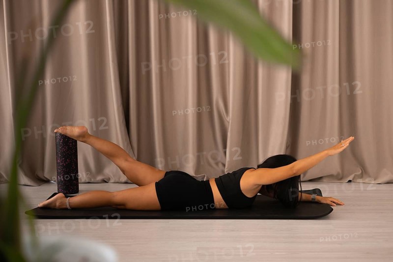 Woman balancing on foam roller in a yoga pose amidst a serene setting