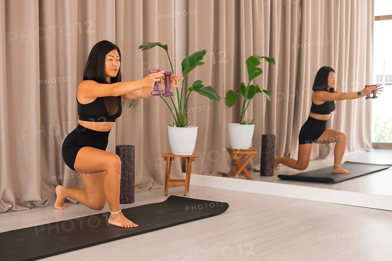 A woman kneels with dumbbells in an indoor setting, practicing her fitness routine