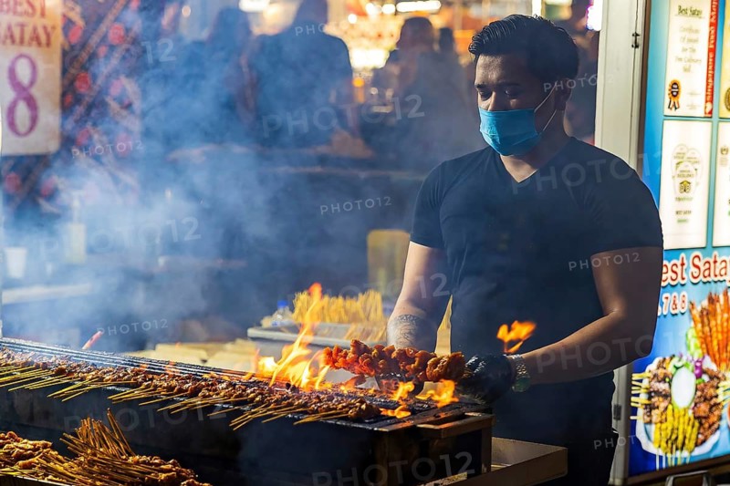 Street food vendor turns and glazes satay skewers over open flames at Satay Street night market, Lau Pa Sat, Singapore