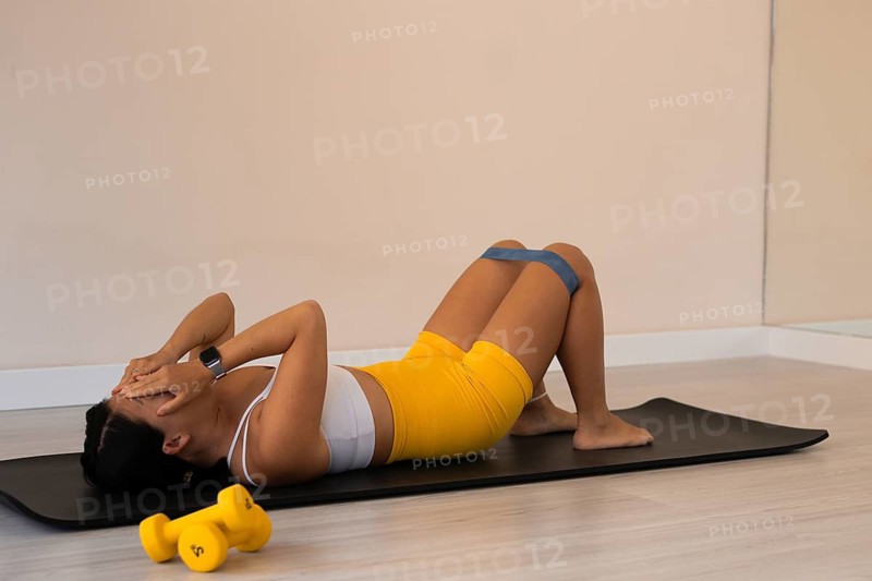Woman lying on an exercise mat resting with hands on face in a workout setting