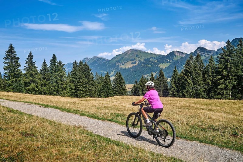Active senior woman rides an e-mountain bike on a picturesque mountain trail under the Nagelfluh Mountains, Oberstaufen, Allgäu, Bavaria, Germany