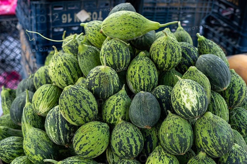 Cluster of striped green gourds stacked in black baskets at market