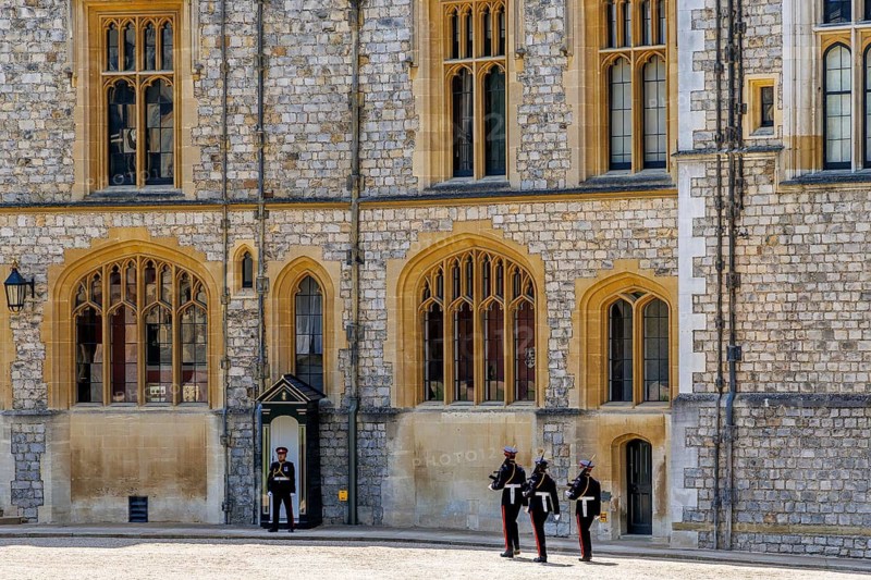 Soldiers in ceremonial uniform parade in front of Windsor Castle's State Apartments during the Changing of the Guard, a ceremony that continues centuries of military tradition alongside the castle's operational role as a royal residence, Windsor, England, United Kingdom