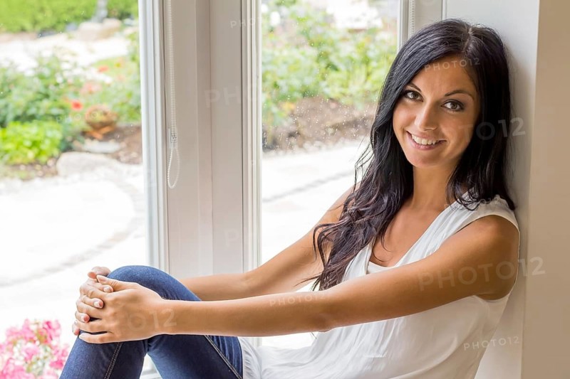 A young dark-haired woman sitting at the window and relaxing, studio shot, 25 years