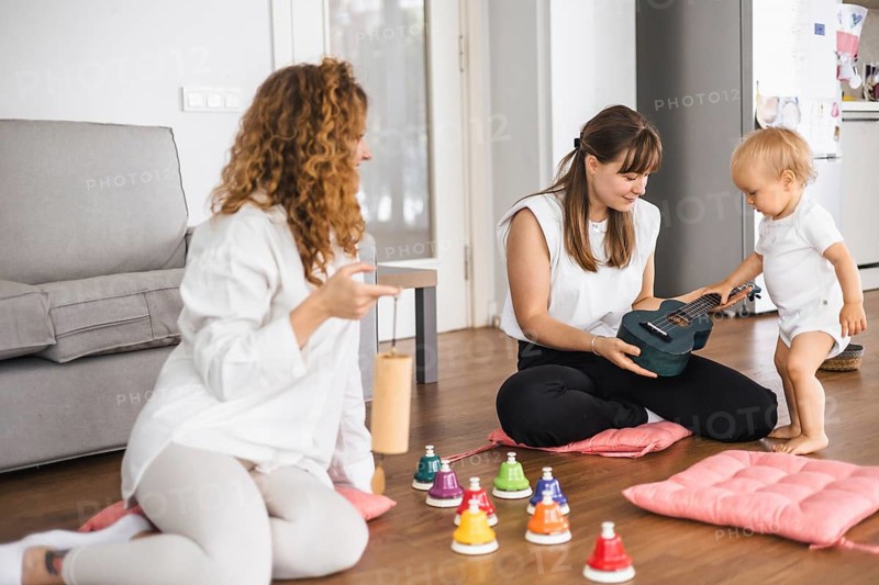 A toddler exploring music with a ukulele and colorful bells in a home setting
