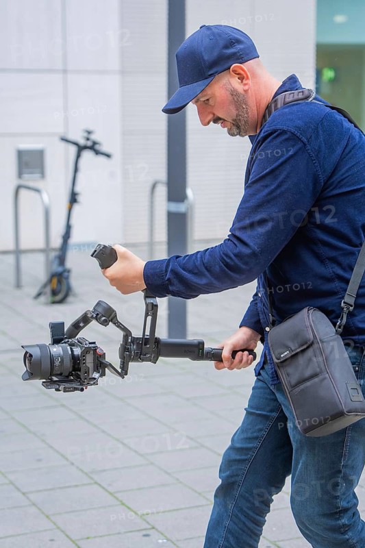 Man operates a camera with gimbal outdoors in front of a building, Milaneo, Stuttgart, Germany