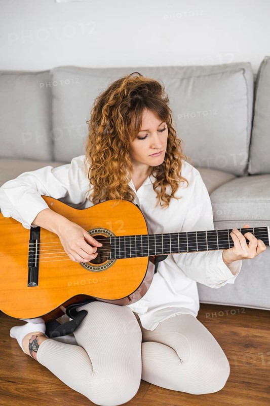 Woman sitting on the floor at home, playing an acoustic guitar in a relaxed manner