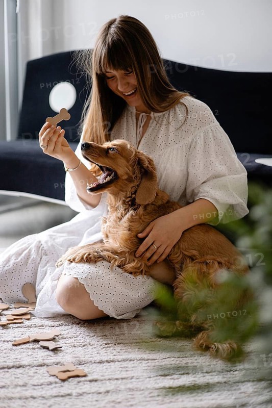 Woman in a white dress laughing with a dog cocker spaniel and puzzle pieces surrounding them