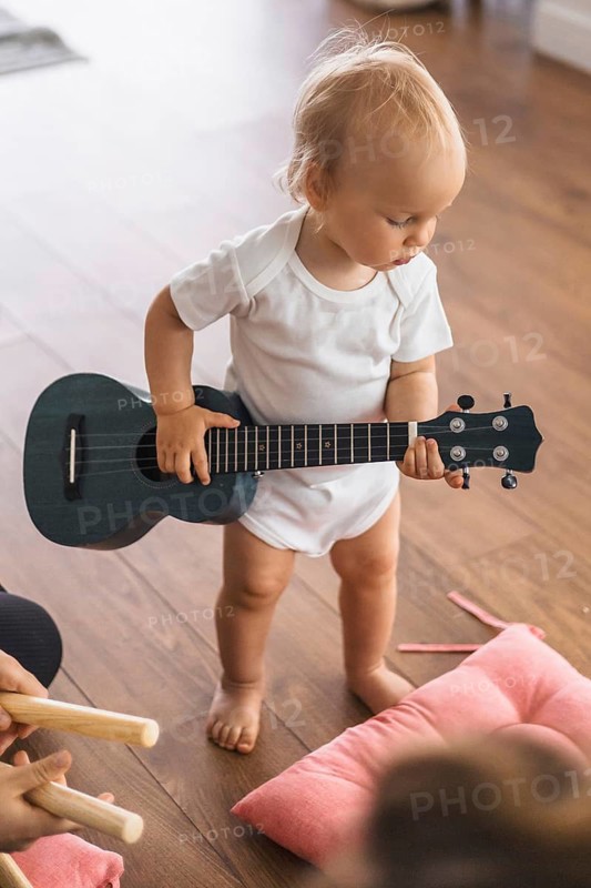 Child holding a guitar, focused on playing, on a wooden floor
