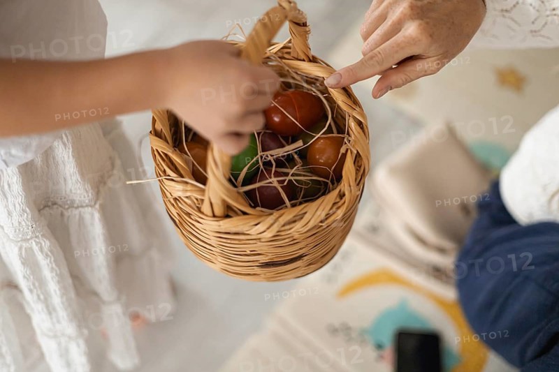 A childs hand reaches for a woven basket filled with colorful eggs. The scene captures a warm, family-oriented atmosphere at home, evoking sensory experiences